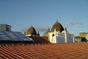 Eine Stadtansicht mit Gebäuden im Vordergrund und einem blauen Himmel im Hintergrund, mit Solarpanelen auf dem Dach eines Gebäudes.