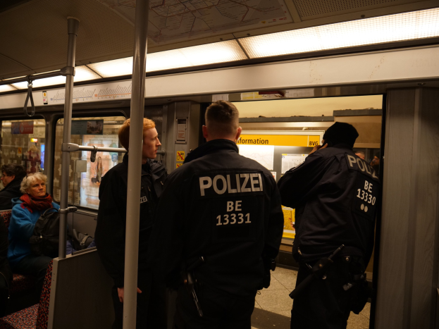 Eine Gruppe von Polizisten steht neben sitzenden und stehenden Passagieren auf einem hell erleuchteten U-Bahn-Zug.