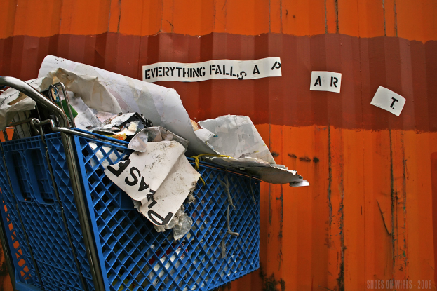 Blauer Einkaufswagen voller Papiere auf einem Metallbehälter mit Text und einem Wasserzeichen in der rechten unteren Ecke.