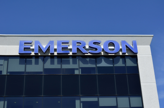 Emerson-Logo an einer Gebäudeseite mit dem Text "Emerson investiert 1,5 Milliarden USD in den USA" vor einem klaren blauen Himmel.