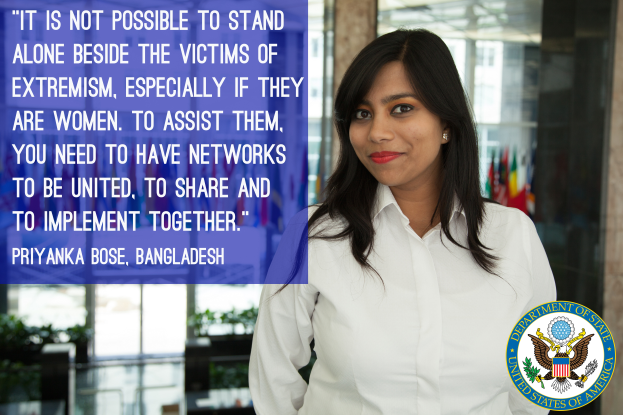 Eine Frau in einem weißen Hemd steht vor einem Gebäude mit einer Aussage über Einheit und Unterstützung für Opfer von Extremismus, insbesondere Frauen, mit einem Logo in der rechten unteren Ecke.