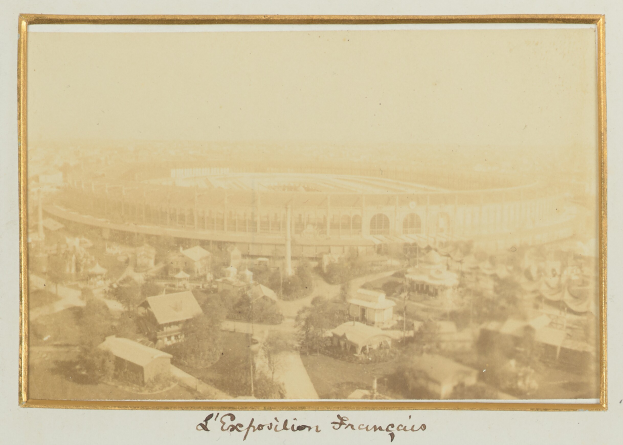 Altes Foto eines Stadions umgeben von Gebäuden, Bäumen und Pfählen mit Text unten.