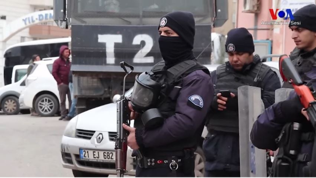 Eine Gruppe von Polizisten in Uniform mit Waffen steht zusammen auf einer Straße während einer Anti-Regierungsdemo in Ankara, Türkei, mit Fahrzeugen, Menschen, Gebäuden und Texttafeln im Hintergrund.