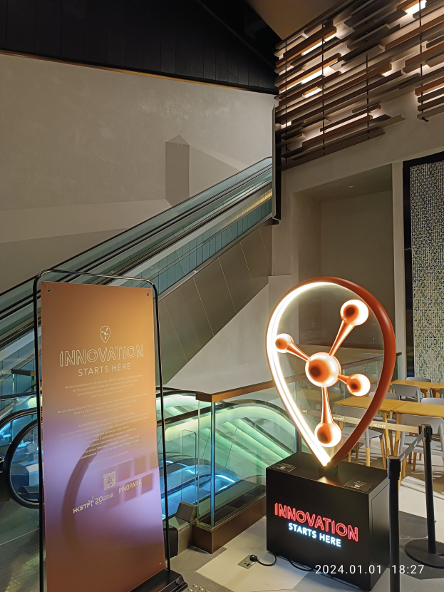 Großes Schild mit der Aufschrift "Innovation Starts Here" in einem Gebäude mit einer Rolltreppe im Hintergrund, Tischen und Stühlen rechts und einem HSTP20 Expo-Schild links.
