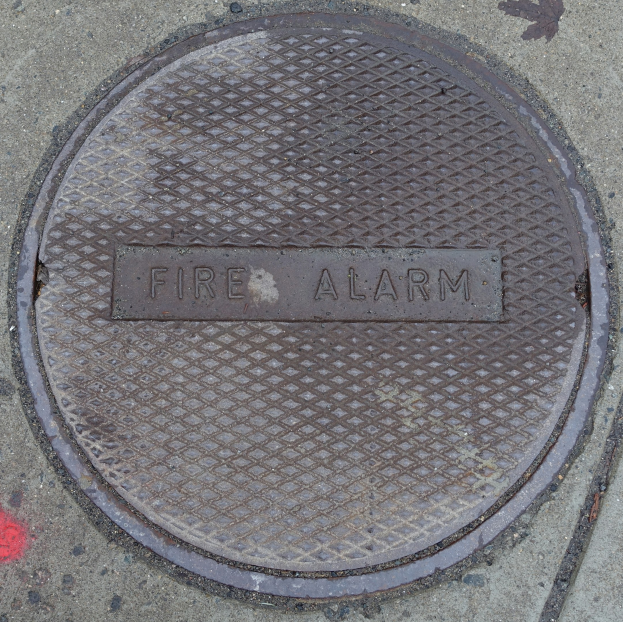 Metall-Schachtobel auf dem Gehweg mit der Aufschrift "Feueralarm"