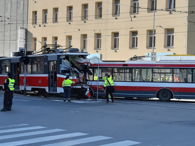 Rote und weiße Tram, die auf der Seite liegt, mit Menschen in der Nähe und einem Gebäude im Hintergrund.