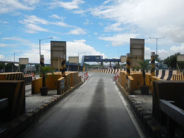 Straße mit einer Mäßstation, Barrieren, Verkehrskegel, Topfpflanzen, Schilder, Straßenlaternen, Bäume und eine Brücke.