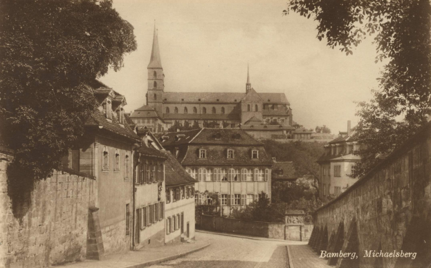 Altes Schwarz-Weiß-Foto einer Stadtstraße in Bamberg, Deutschland, mit einer Kirche im Hintergrund, Mauern auf beiden Seiten, Bäumen, die die Straße säumen, und sichtbarem Himmel darüber.