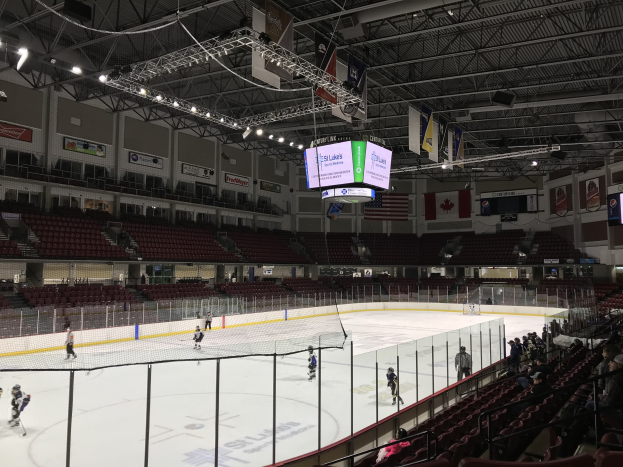 Eishockeyspiel in einer großen Arena mit einem zentralen Netz, Zuschauern auf Stühlen, Deckenbeleuchtung und Trägern sowie Bannern an den Wänden, identifiziert als die St. Louis Blues Arena.