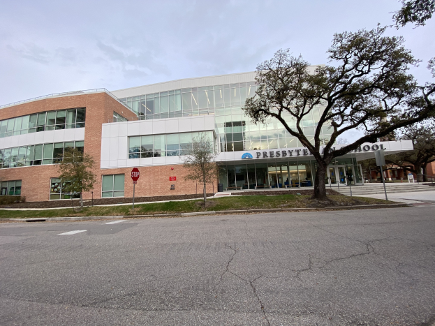 Großes zweistöckiges Backsteingebäude mit der Aufschrift "Presbyte Middle School" und vielen rechteckigen Fenstern, umgeben von Bäumen, Gras, Schildern, Strommasten und einer asphaltierten Straße unter einem bewölkten Himmel.