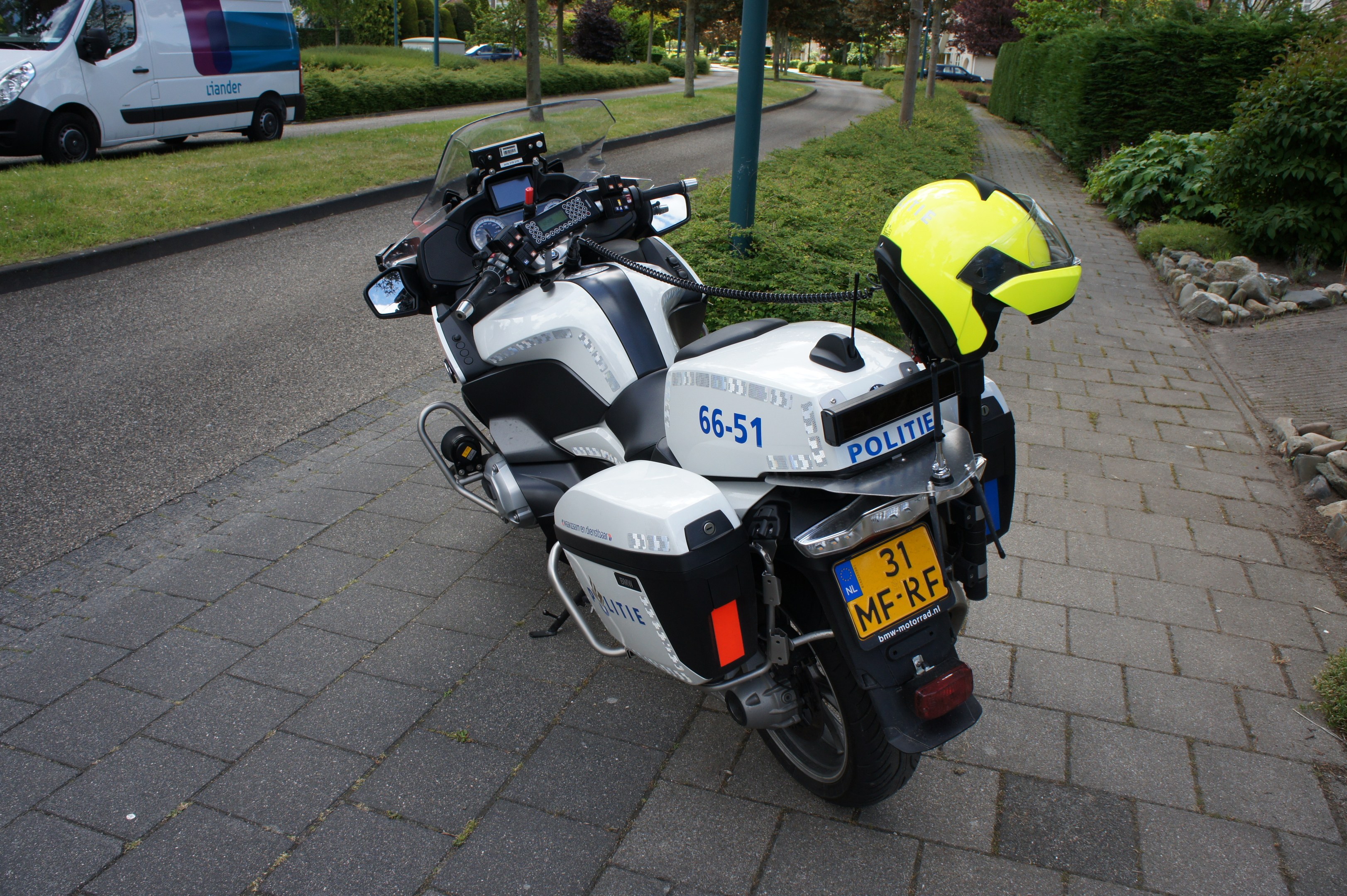 Polizeimotorrad am Straßenrand mit Helm darauf, Bäume und Gebäude im Hintergrund.