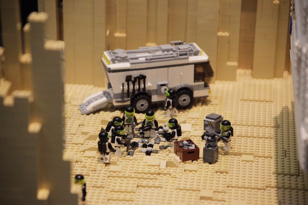Lego-Modell einer Star-Wars-Szene mit einem Fahrzeug im Vordergrund und einer Wand im Hintergrund sowie verstreuten Lego-Spielzeugen.