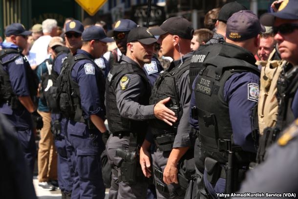 Eine Gruppe von Polizisten in Uniform auf der Straße, einige mit Waffen, mit Gebäuden und Schildern im Hintergrund.