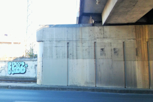 Betonwand mit Graffiti, Straße am Boden, fernes Gebäude, Turm und klarer blauer Himmel.