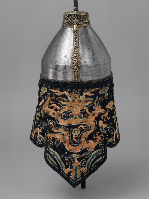 Metallhelm mit einer Drachengestaltung auf einem grauen Hintergrund.