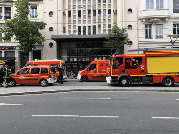 Eine Gruppe von Feuerwehrautos auf einer Straße in Paris geparkt mit Menschen in der Nähe, vor Häusern, Bäumen und einem Fahrrad im Hintergrund.