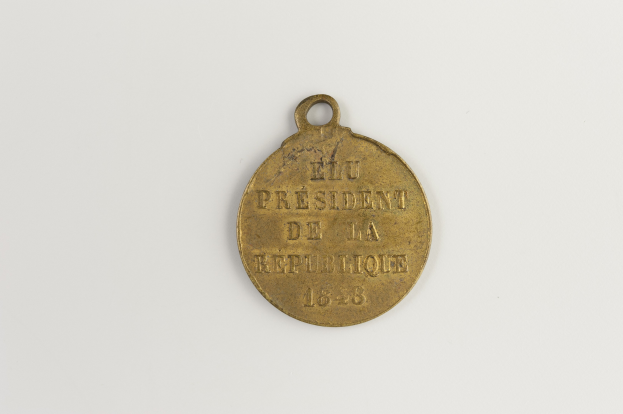 Goldmedaille mit 'Präsident der Republik' eingraviert, in der Mitte eines weißen Hintergrunds.