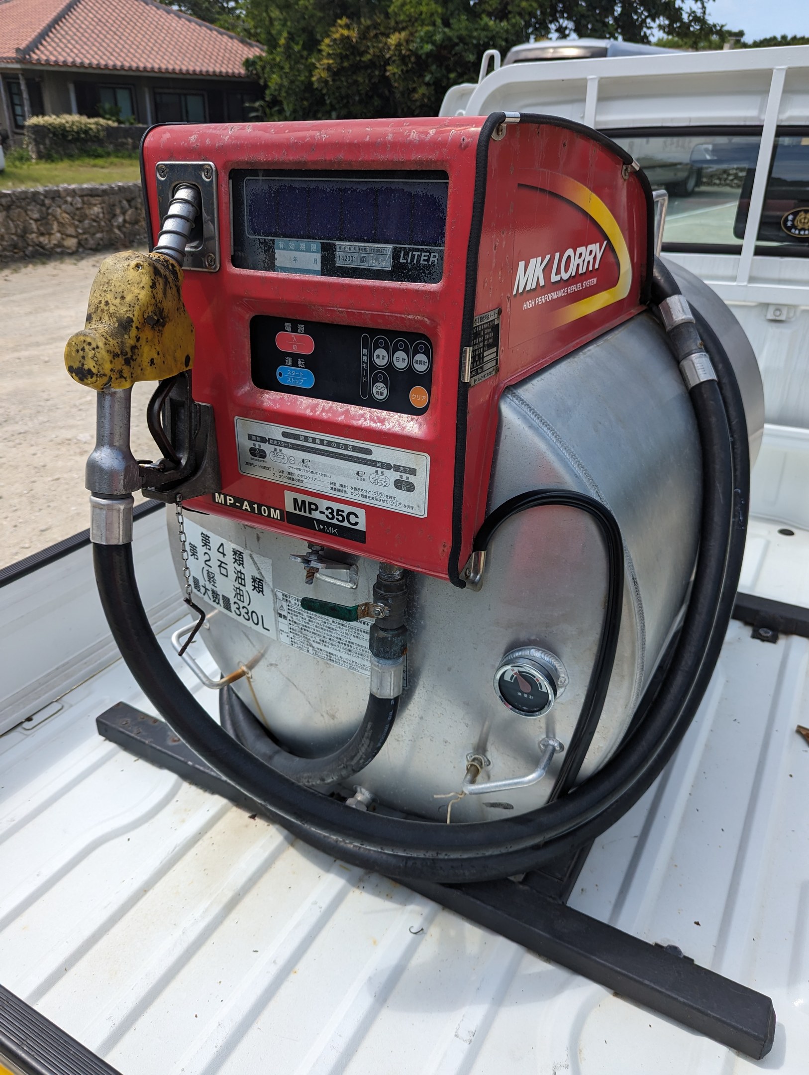 Ein Lkw mit einer angebauten Benzinpumpe, der Fahrzeuge in einem Wohngebiet unter einem klaren blauen Himmel betankt.