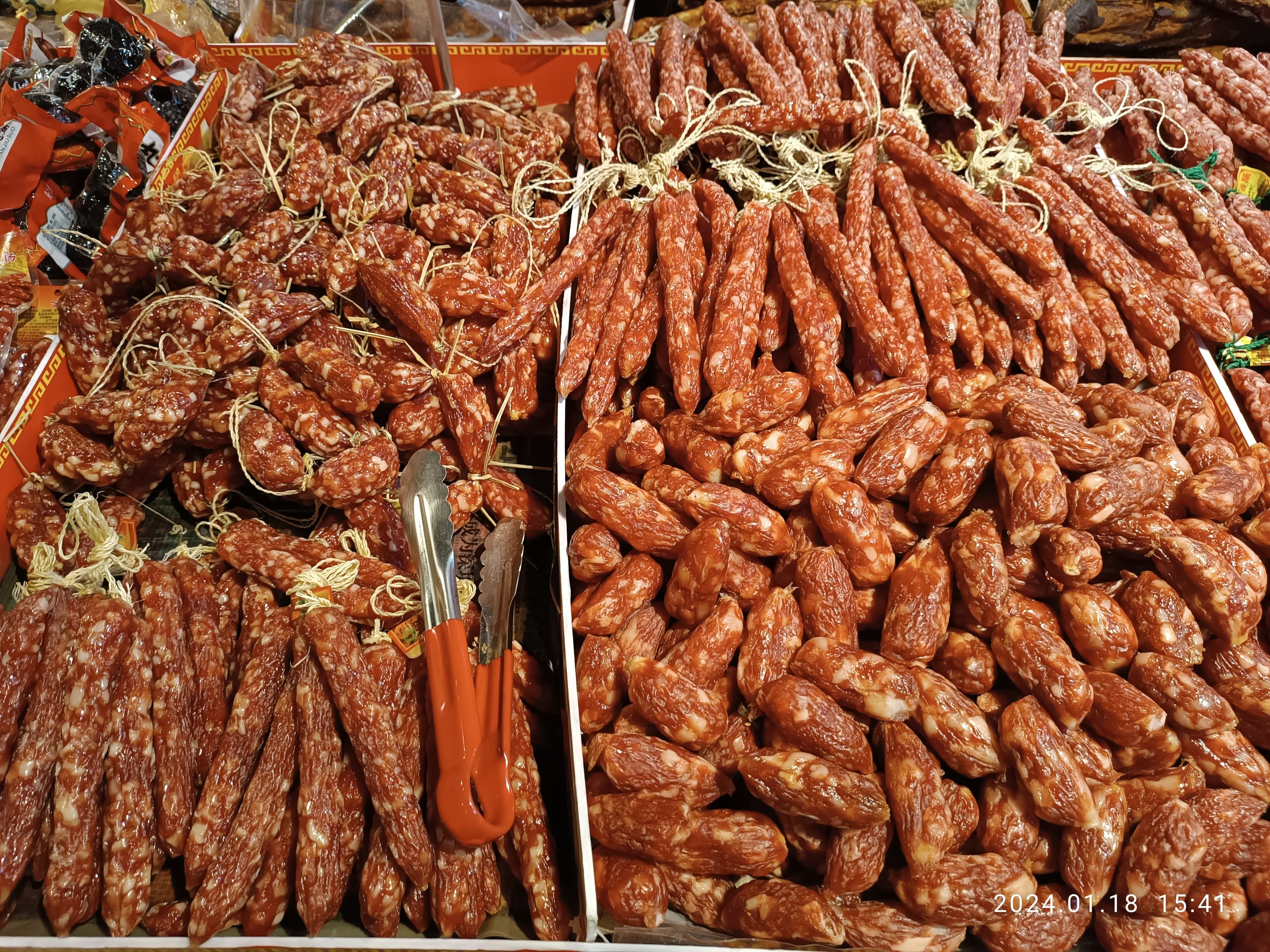 Marktbodenständer mit verschiedenen Wurstwaren, verpackten Lebensmitteln und anderen Artikeln, mit einem Wasserzeichen.