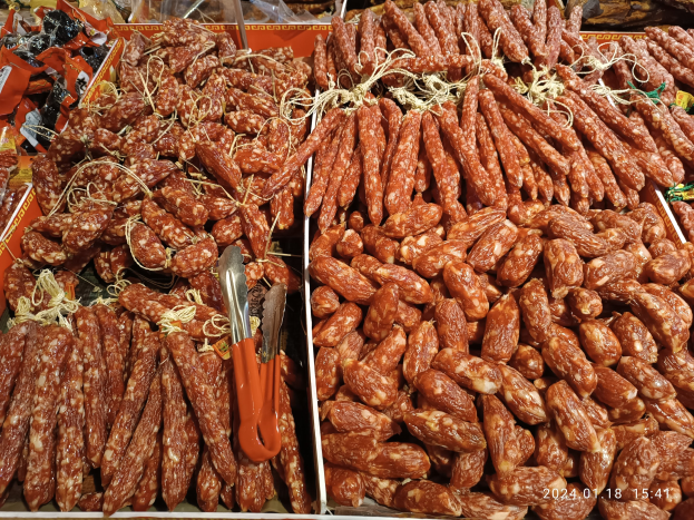 Marktbodenständer mit verschiedenen Wurstwaren, verpackten Lebensmitteln und anderen Artikeln, mit einem Wasserzeichen.