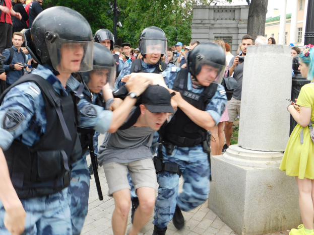 Gruppe von Einsatzpolizisten in Ausrüstung, die vor einer Menge davonläuft, einige bewaffnet, mit einer Säule im Vordergrund, Bäumen, Gebäuden und Laternen im Hintergrund, Kiew, Ukraine.