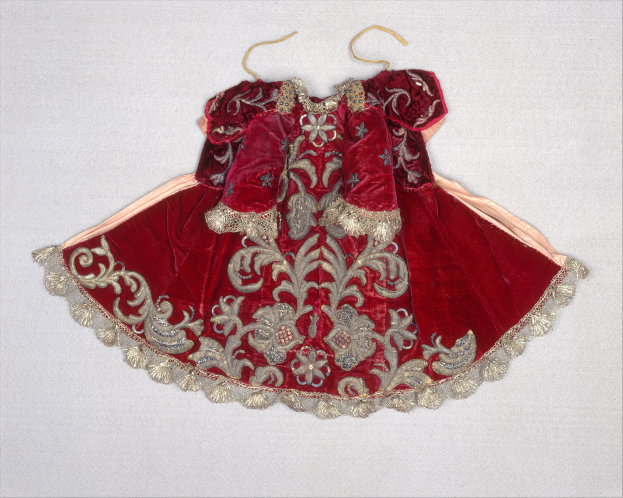 Ein rotes Samtkleid mit goldener Stickerei, das an einem Bügel gegen einen weißen Hintergrund hängt, mit aufwändigen und luxuriösen Designs.