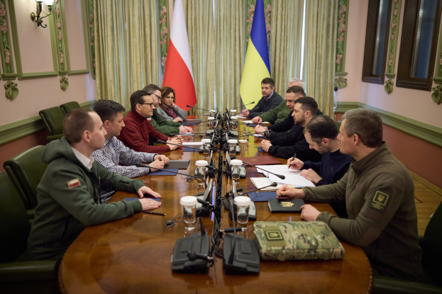 Eine Gruppe von Männern in einer offiziellen Umgebung mit Mikrofonen und Dokumenten an einem Holztisch, die eine Vereinbarung diskutieren.