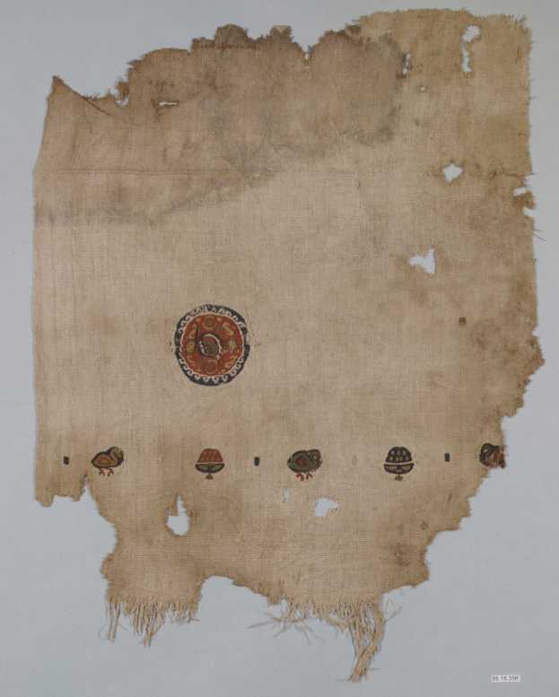 Ein Stück Stoff mit einem leuchtenden, detailreichen kreisförmigen Design aus verschiedenen Formen und Farben, einschließlich Kreisen, Quadraten und Dreiecken, vor einem weißen Hintergrund.