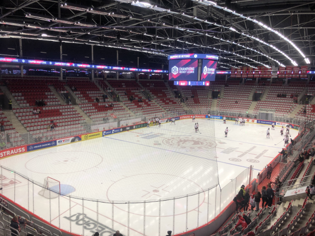 Ein Hockey-Spiel in einer großen Arena mit Zuschauern auf den Sitzplätzen und einigen Stehplätzen, einem Zaun um die Eisfläche, einem Display mit der Aufschrift "St. Louis Blues vs Detroit Red Wings", Metallrahmen und einer Decke mit Deckenleuchten.
