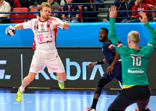 Eine Gruppe von Männern, die Handball auf einem Court spielen, mit einem Ball in der Mitte, während Zuschauer von Stühlen und Geländern in einem Stadion zusehen, mit einem Schild, auf dem "Futsal World Cup 2019 - Bayern Munich vs Paris Saint-Germain" steht.