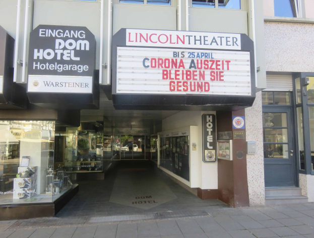Außenansicht des Lincoln Theaters in Berlin, Deutschland, mit Glasfenstern und -türen und einer Texttafel, die ein geschäftiges Inneres mit verschiedenen Gegenständen zeigt.