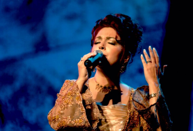 Eine Frau in einem goldenen Kleid, die in ein Mikrofon singt, auf einer Bühne beim Eurovision Song Contest mit einem blauen und schwarzen Hintergrund.