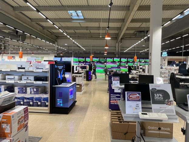 Großer Raum voller Elektronik in Regalen angeordnet, darunter Computer und Drucker, mit Menschen auf dem Boden, einer Säule, Schildern, Deckenleuchten und Deckenventilatoren, in einem kürzlich eröffneten Walmart-Geschäft.