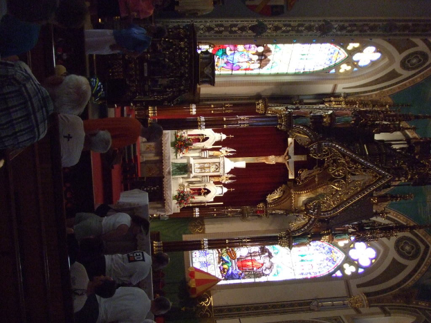 Ein Innenblick in eine Kirche mit einem Kreuz, das eine Jesus-Skulptur und zahlreiche vor ihr sitzende Menschen zeigt.