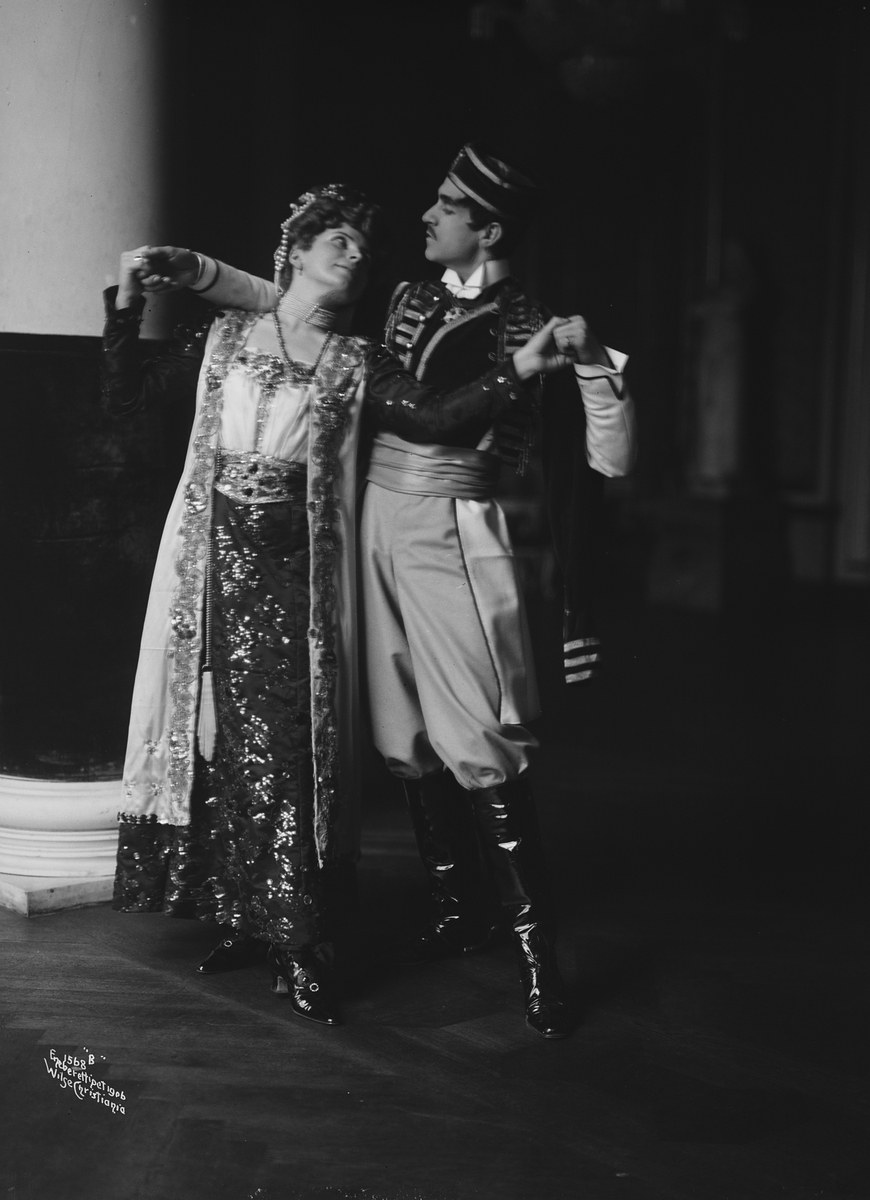 Schwarz-weiß-Foto eines Mannes und einer Frau, die in einem Ballsaal tanzen, mit einer Säule und einer Wand im Hintergrund, der Mann trägt Schuhe während einer Vorstellung.