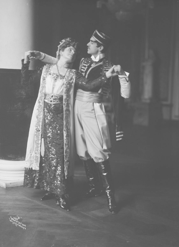 Schwarz-weiß-Foto eines Mannes und einer Frau, die in einem Ballsaal tanzen, mit einer Säule und einer Wand im Hintergrund, der Mann trägt Schuhe während einer Vorstellung.