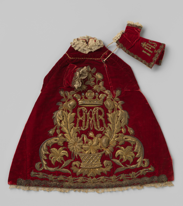 Ein roter Samtmantel mit goldener Stickerei und einer Krone-Motiv, vor einem weißen Hintergrund.