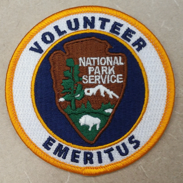 Runder Flicken mit "Volunteer National Park Service Emeritus" in schwarzer Schrift auf weißem Hintergrund, umrandet von einem blauen Rand und einem gelben Kreis.
