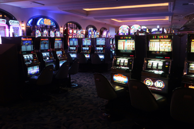 Reihe von Spielautomaten in einem Casino mit Stühlen auf dem Boden und Deckenlampen, Maschinen mit Text und Zahlen, die darauf hinweisen, dass sie zum Verkauf stehen.