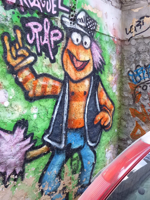 Ein rotes Auto, das vor einer Wand mit Graffiti geparkt ist.