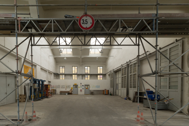 Lagerhalle mit ausführlichem Gerütz, Verkehrskegeln, Metallstäben, einem Schild, Maschinen, einer Tür, Fenstern, Wänden, Deckenleuchten und einem Dach.