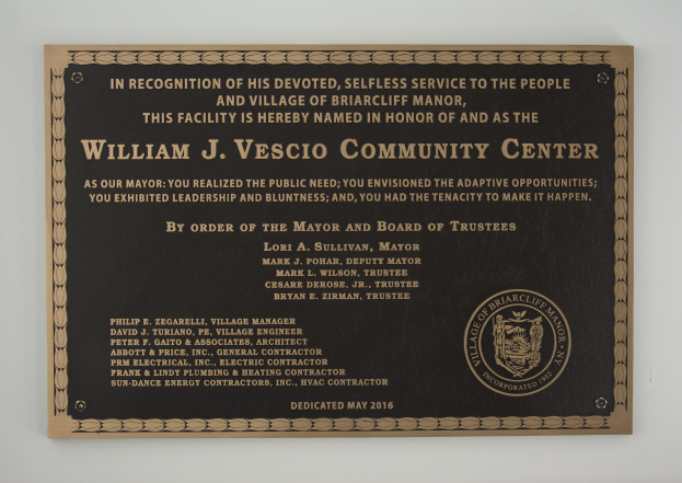 Schwarzes rechteckiges Schild mit weißer fettgedruckter Schrift, die "William J. Vesco Community Center" lautet, an einer Gebäudewand angebracht.