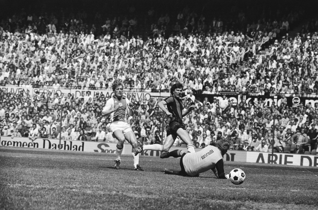 Schwarzes und weißes Foto von Fußballspielern im Einsatz auf einem Feld mit Zuschauern im Hintergrund und einer Bundesliga 1978-79 Ajax 1-1 Hannover 96-Fahne.