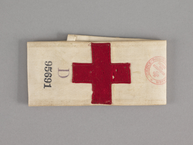 Ein rotes Kreuz-Ersthilfeset in einem Stoffbeutel mit Text und einem Stempel, das auf einer Oberfläche liegt.