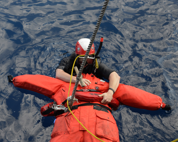 Retter in roter Schwimmweste und Helm im Wasser mit einem Sicherheitsseil befestigt.