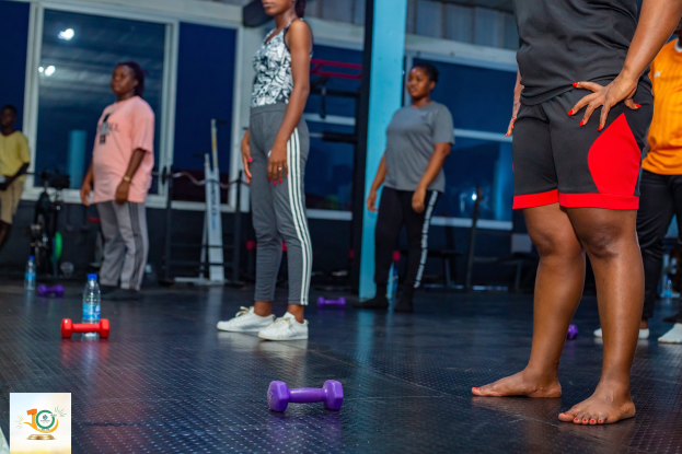 Gruppe von Menschen in einem Fitnessstudio mit Hanteln und Flaschen auf dem Boden, die an einem Fitnesskurs mit Glasfenstern und Lichtern im Hintergrund teilnehmen.