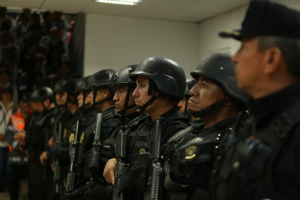 Gruppe von Polizisten in Helmen und Uniformen mit Waffen in der Hand, die vor einer Wand mit Deckenbeleuchtung stehen.