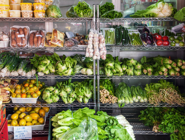 Frische Obst- und Gemüseabteilung in einem Supermarkt mit verpackten Artikeln, Kartons und einer Tafel, im Hintergrund ein Glasfenster.