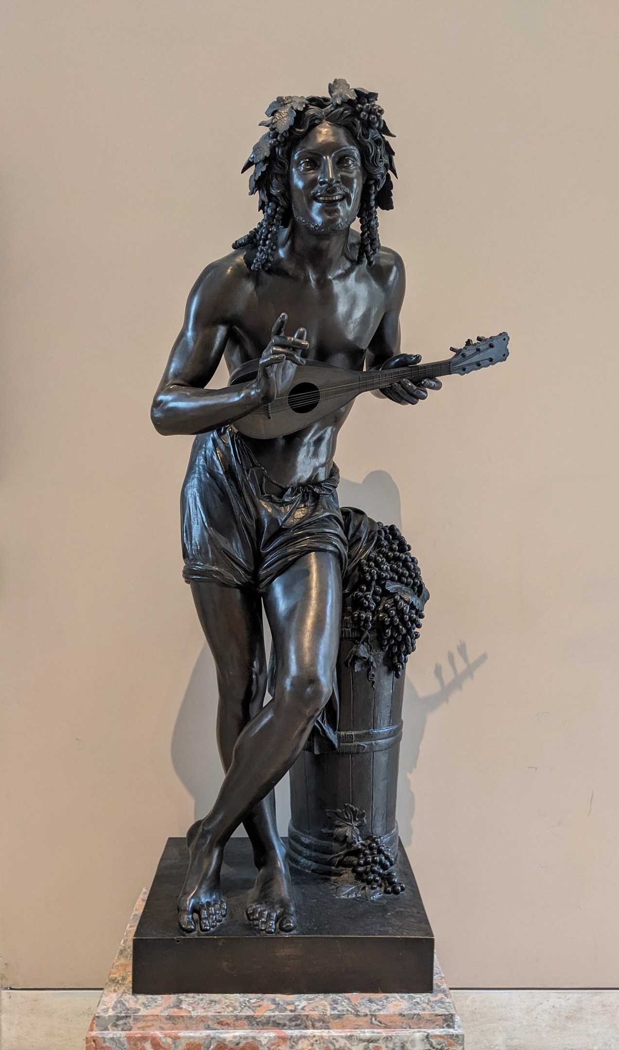 Bronzestatue eines Mannes, der eine Gitarre spielt, mit einer Wand und einem Boden im Hintergrund.